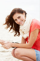 A brunette woman on a beach wearing a scarf and a salmon-coloured top