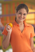 Junge brünette Frau im orangenem Poloshirt hält eine Orange