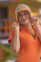 A young brunette woman wearing an orange polo shirt with a colourful summer hat