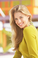 A young blonde woman on a beach wearing an olive top