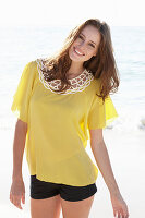 Junge brünette Frau im gelben Sommerkleid und schwarzer Shorts am Strand