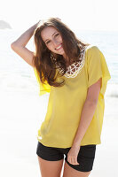 A young brunette woman on a beach wearing a yellow summer dress and black shorts