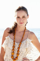 Junge brünette Frau im hellen Sommerkleid und Halskette am Strand