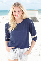 Junge blonde Frau in blauem Langarmshirt und Shorts am Strand