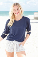Junge blonde Frau in blauem Langarmshirt und Shorts am Strand