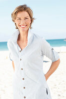 A mature woman with short blonde hair on a beach wearing a light-blue striped short