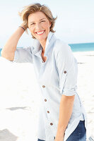 A mature woman with short blonde hair on a beach wearing a light-blue striped short