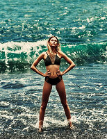 A young blonde woman on a beach wearing a black bikini