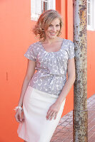 A blonde woman wearing a grey spotted blouse and a white skirt