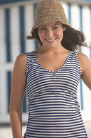 A young brunette woman on a beach wearing a blue-and-white striped top and a summer hat