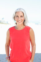 A mature woman with white hair on a beach wearing a red top