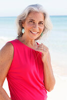 A mature woman with white hair on a beach wearing a pink top