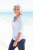 Reife Frau mit weißen Haaren in gestreifter Bluse, Top und Bluejeans am Strand