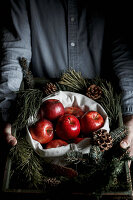 Mann hält Korb mit Reisig und roten Äpfeln