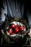 A man holding a basket of brushwood and red apples