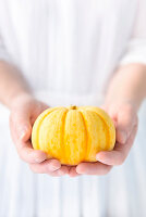 A woman holding a yellow pumpkin in both hands