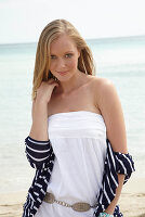 Junge Frau in weißem Sommerkleid und gestreiftem Jäckchen am Strand