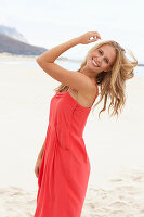 A young blonde woman on a beach wearing a red summer dress