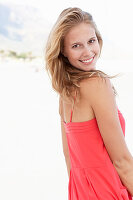 Junge blonde Frau in rotem Sommerkleid am Strand