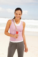 A young brunette woman by the sea wearing sports clothes with a skipping rope