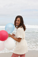 A brunette woman wearing a short-sleeved cardigan and holding balloons