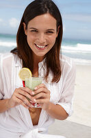Junge brünette Frau mit Smoothie in weißem Hemd am Strand