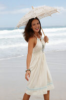 Brünette Frau mit Sonnenschirm in weißem Sommerkleid am Meer