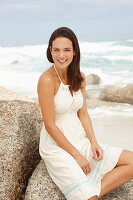 A brunette woman by the sea wearing a white summer dress