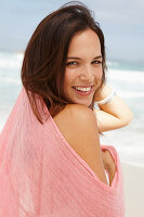 A brunette woman by the sea with a pink shawl
