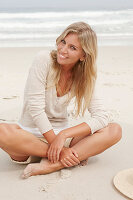 A blond woman on a beach wearing a light cardigan and shorts