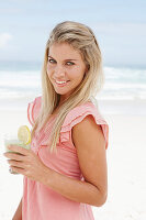 A young woman on a beach with a smoothie wearing a pink top