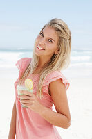 Junge Frau mit Smoothie im rosa Top am Strand