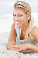 A blonde woman lying on the beach wearing a light t-shirt