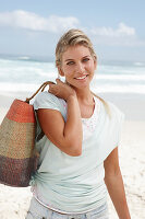 A blonde woman on the beach wearing a light t-shirt and holding a wicker bag