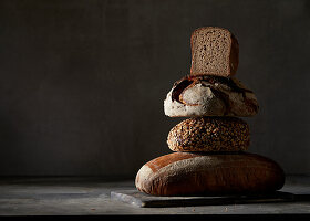 Vier verschiedene Brote, gestapelt vor dunklem Hintergrund