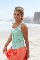 Blonde Frau in türkisgrünem Top und lachsfarbenem Rock am Strand