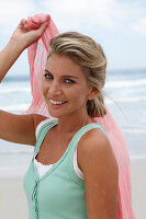 A blonde woman on a beach with a scarf and a turquoise top