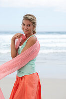 Blonde Frau mit Tuch in türkisgrünem Top und lachsfarbenem Rock am Strand