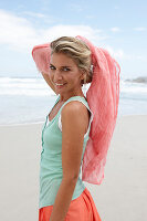 Blonde Frau mit Tuch in türkisgrünem Top und lachsfarbenem Rock am Strand