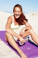 Brünette Frau in Top und Shorts auf Strandmatte sitzend