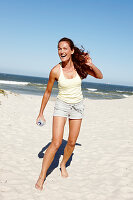 Brünette Frau mit Wasseflasche in hellem Top und Shorts am Strand