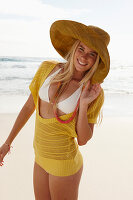 Blonde Frau mit Hut in gelbem Stricktop und Bikini am Strand