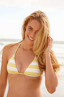 A blonde woman on a beach wearing a white and yellow bikini