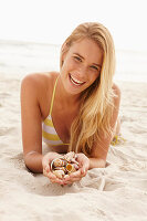 Blonde Frau mit Muschelschalen am Strand liegend