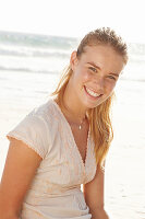 A blonde woman by the sea wearing a white embroidered dress