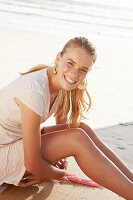 Blonde Frau in weißem Kleid auf Strandmatte am Meer