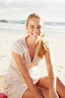 A blonde woman by the sea wearing a white embroidered dress