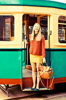 A young blonde woman wearing a jumper and a skirt standing in the door of a tram