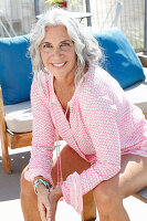 A mature woman wearing a pink blouse sitting on a terrace