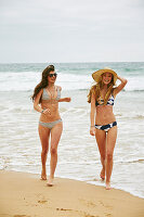 Zwei Frauen in Bikinis und mit Sommerhut an einem Strand